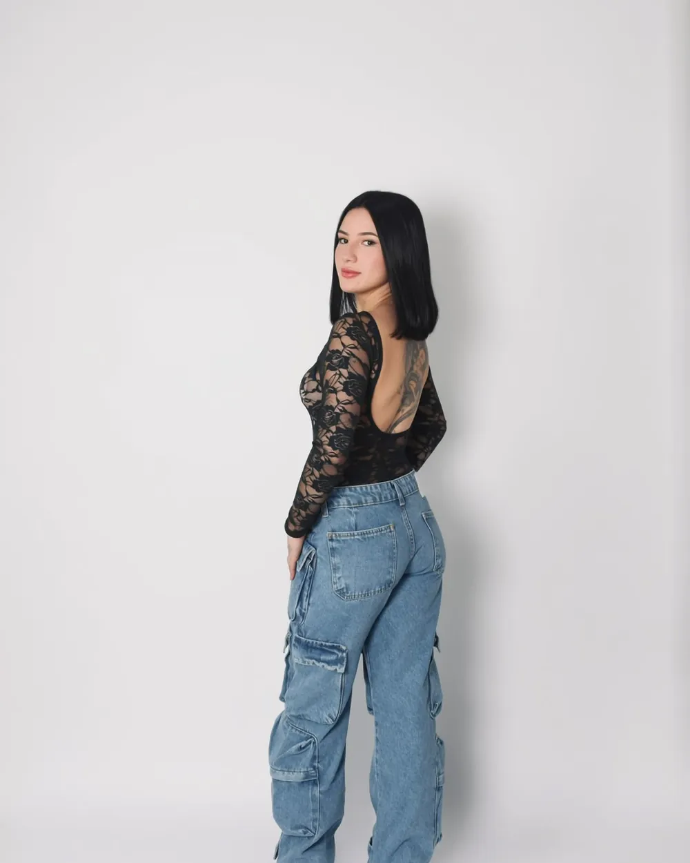 Modelo de costas com body de renda preto e calça cargo jeans azul